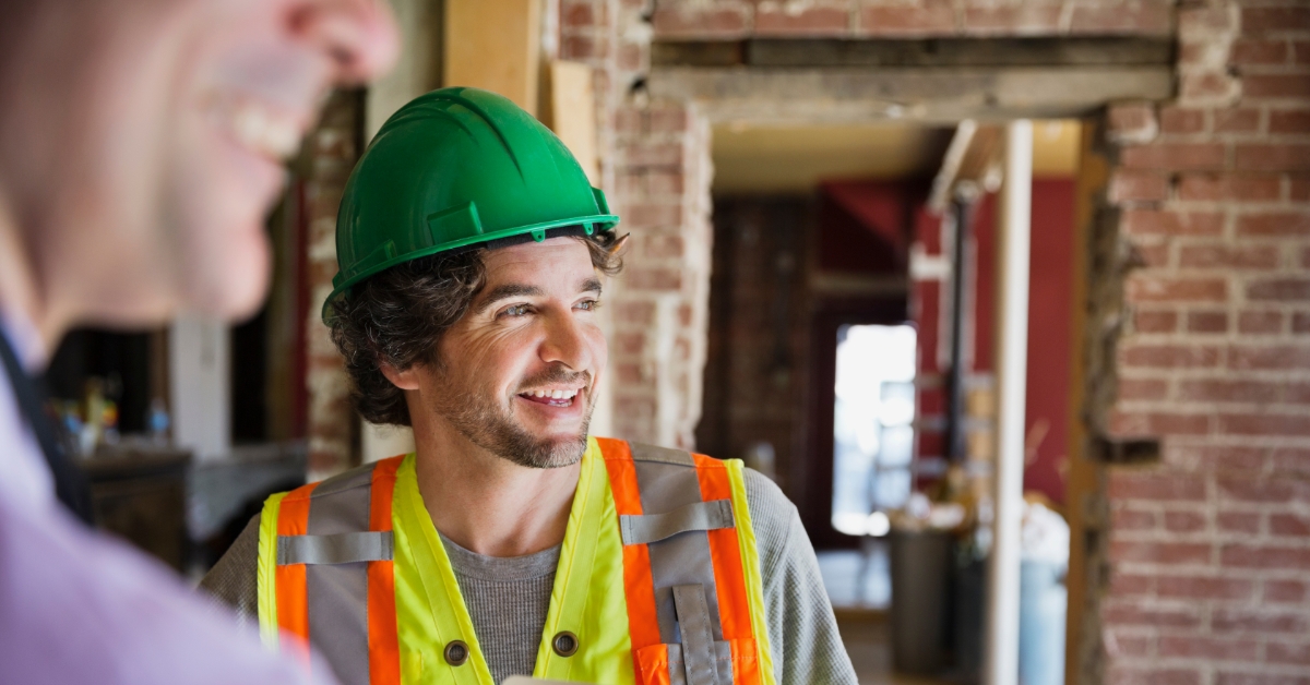 Tradesman in hard hat talking with a colleague inside a house renovation